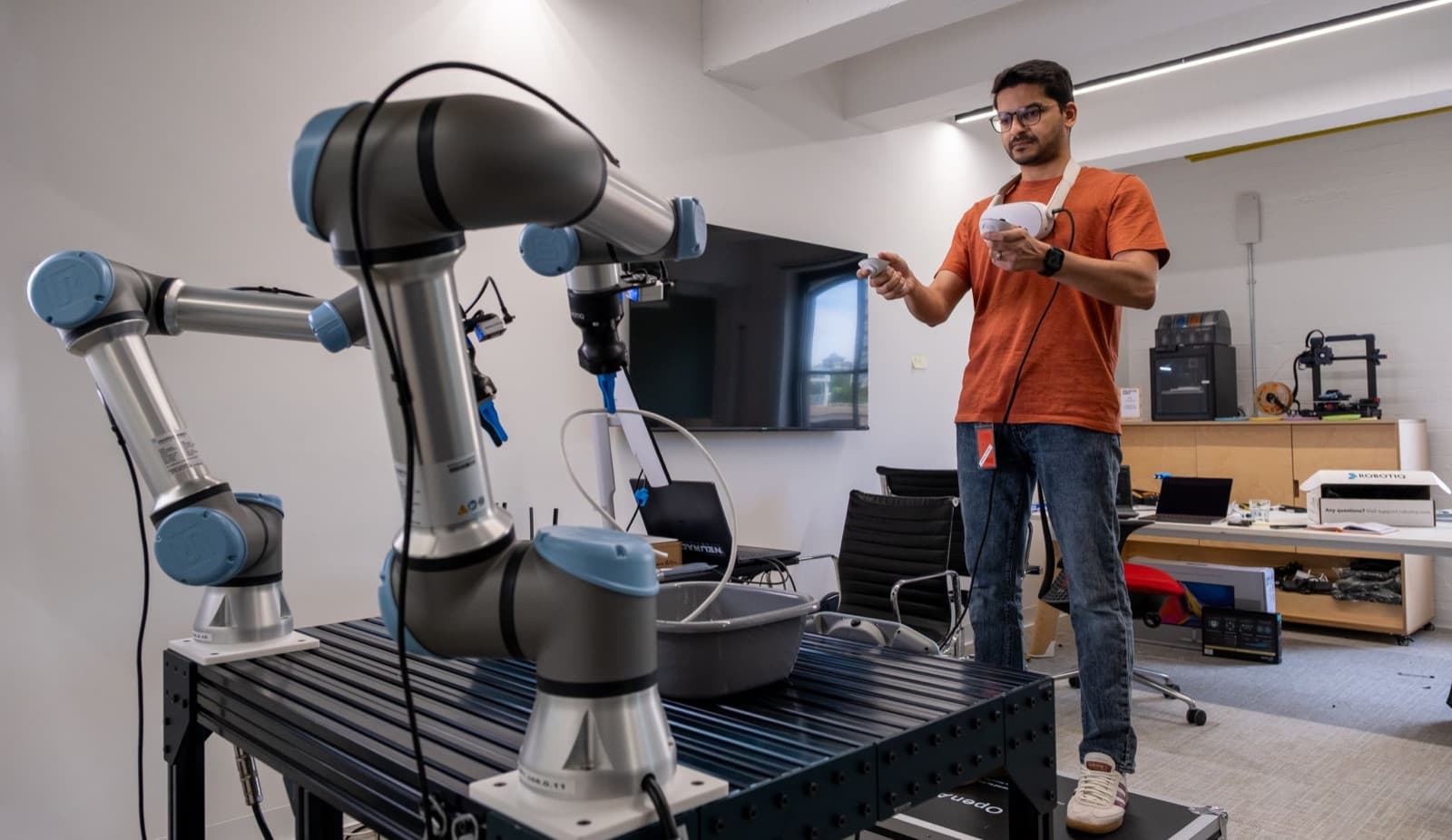 An operator using VR controllers to teleoperate two Universal Robots arms for data collection