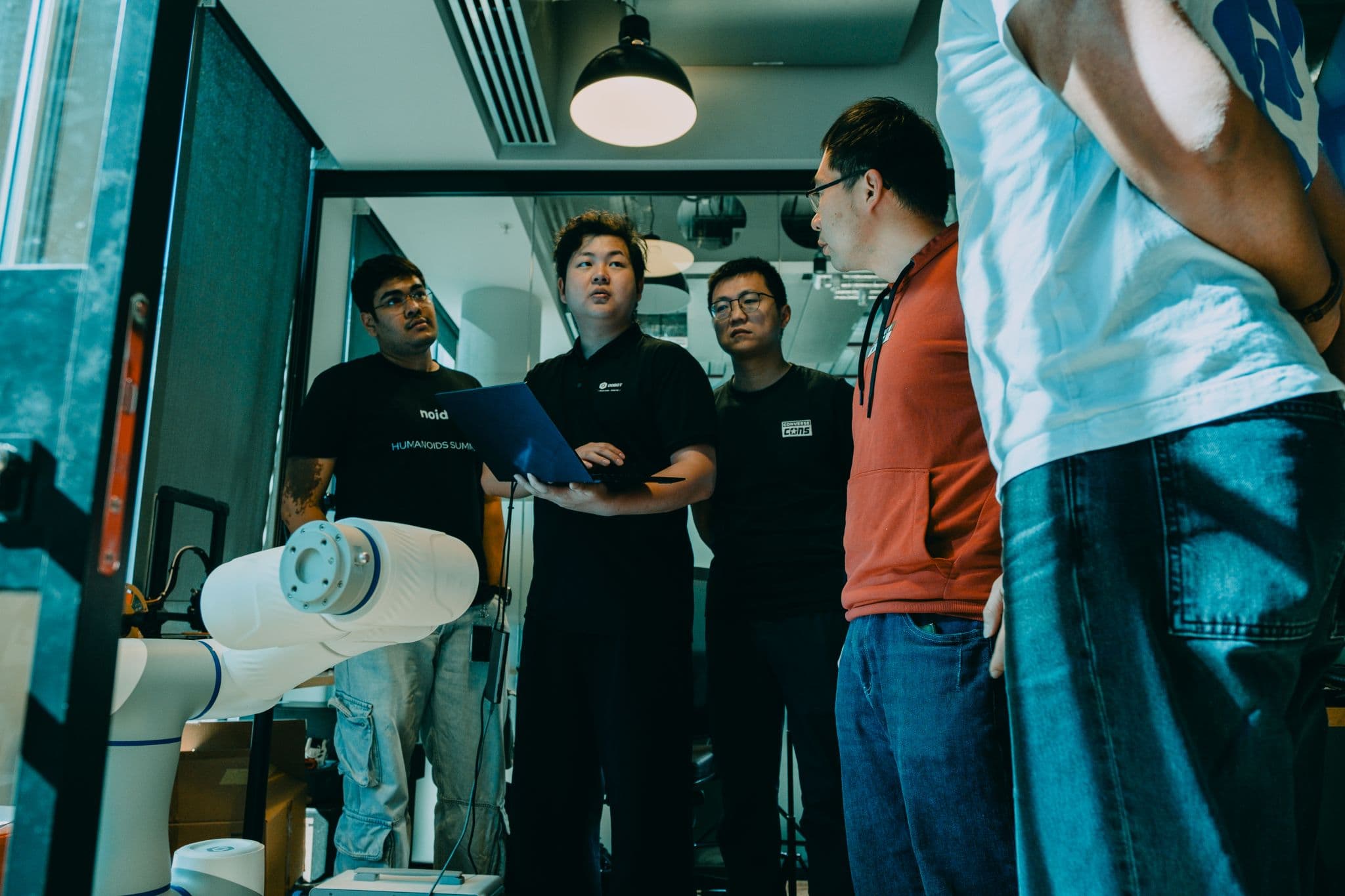 A robotics team gathered around a laptop and a robot arm