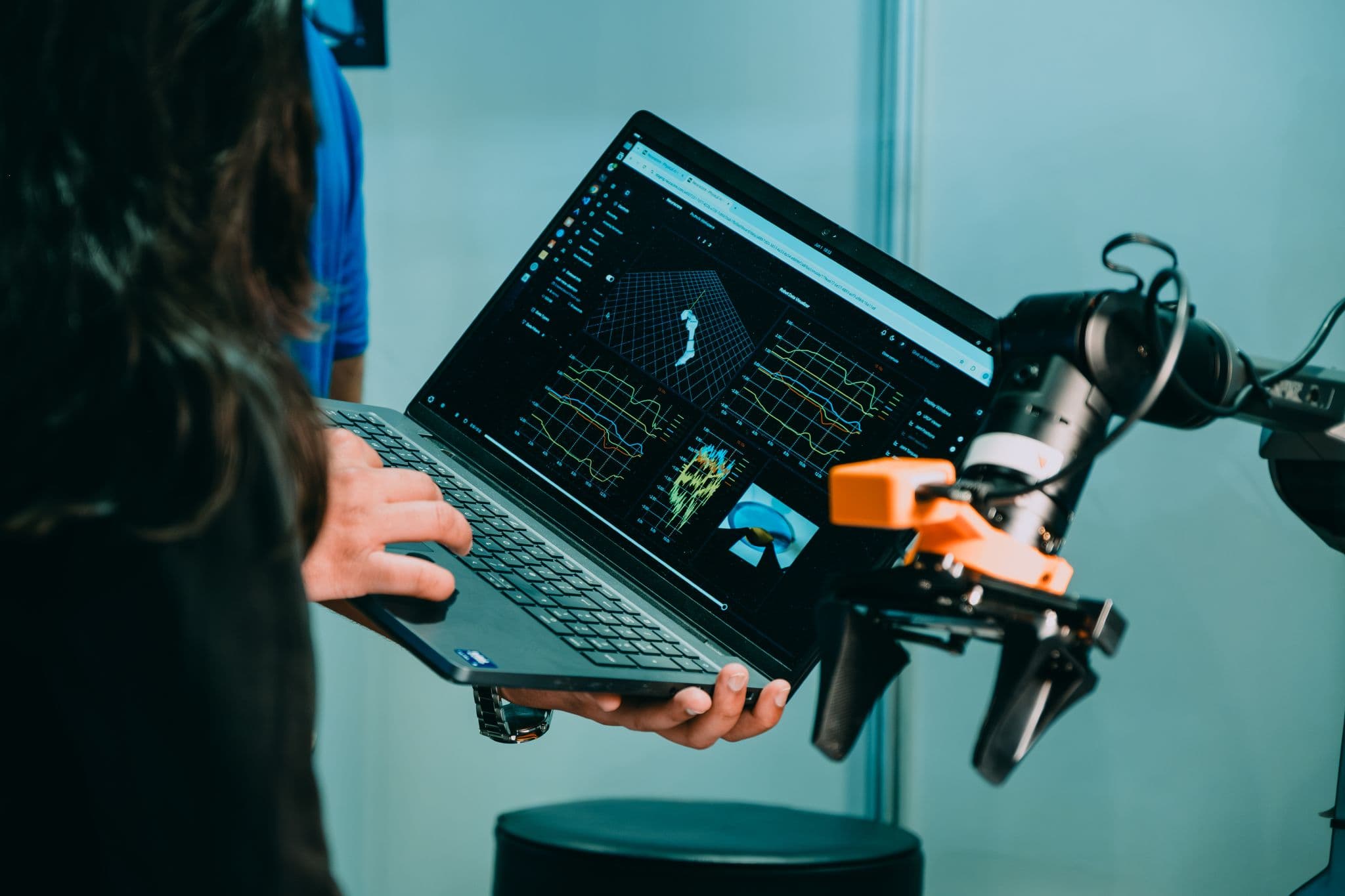 Person holding a laptop showing dashboards next to a robot gripper